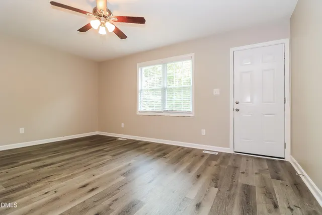 an empty room with wooden floor chandelier fan and windows