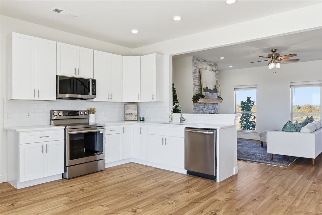 846 Old Tioga Road Gunter, TX 75058 - Photo 8 of 38 a kitchen with stainless steel appliances white cabinets a sink a stove a microwave and wooden floors