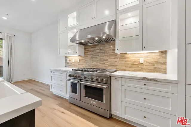 a view of an empty room with wooden floor and a kitchen