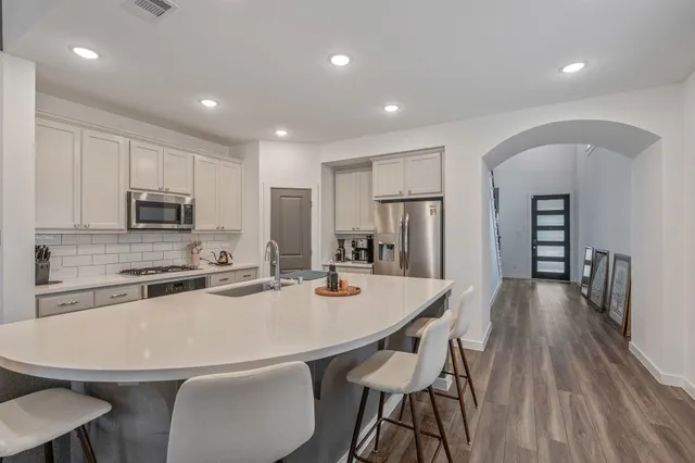 a kitchen with stainless steel appliances a dining table chairs refrigerator and microwave