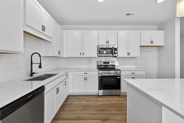 a kitchen with stainless steel appliances granite countertop a sink dishwasher a stove top oven a refrigerator with white cabinets and wooden floor