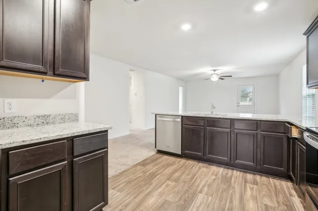 a kitchen with stainless steel appliances granite countertop a sink dishwasher a stove with wooden cabinets and floor