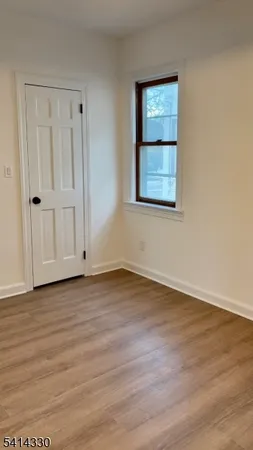 a view of an empty room with wooden floor and window