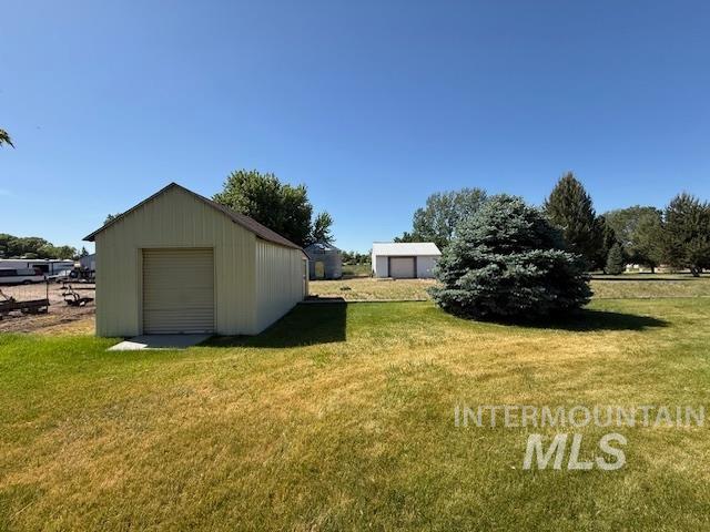 1095 County Road 70 Weiser, ID 83672 - Photo 8 of 44 Metal outbuilding with a single garage door and a sloped roof, complemented by a large evergreen tree in the foreground