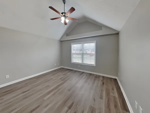 an empty room with wooden floor chandelier fan and windows