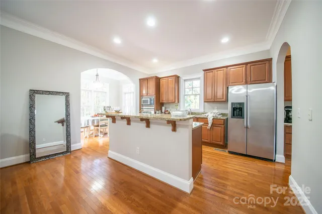a living room with stainless steel appliances granite countertop a refrigerator a sink dishwasher and a stove with wooden floor