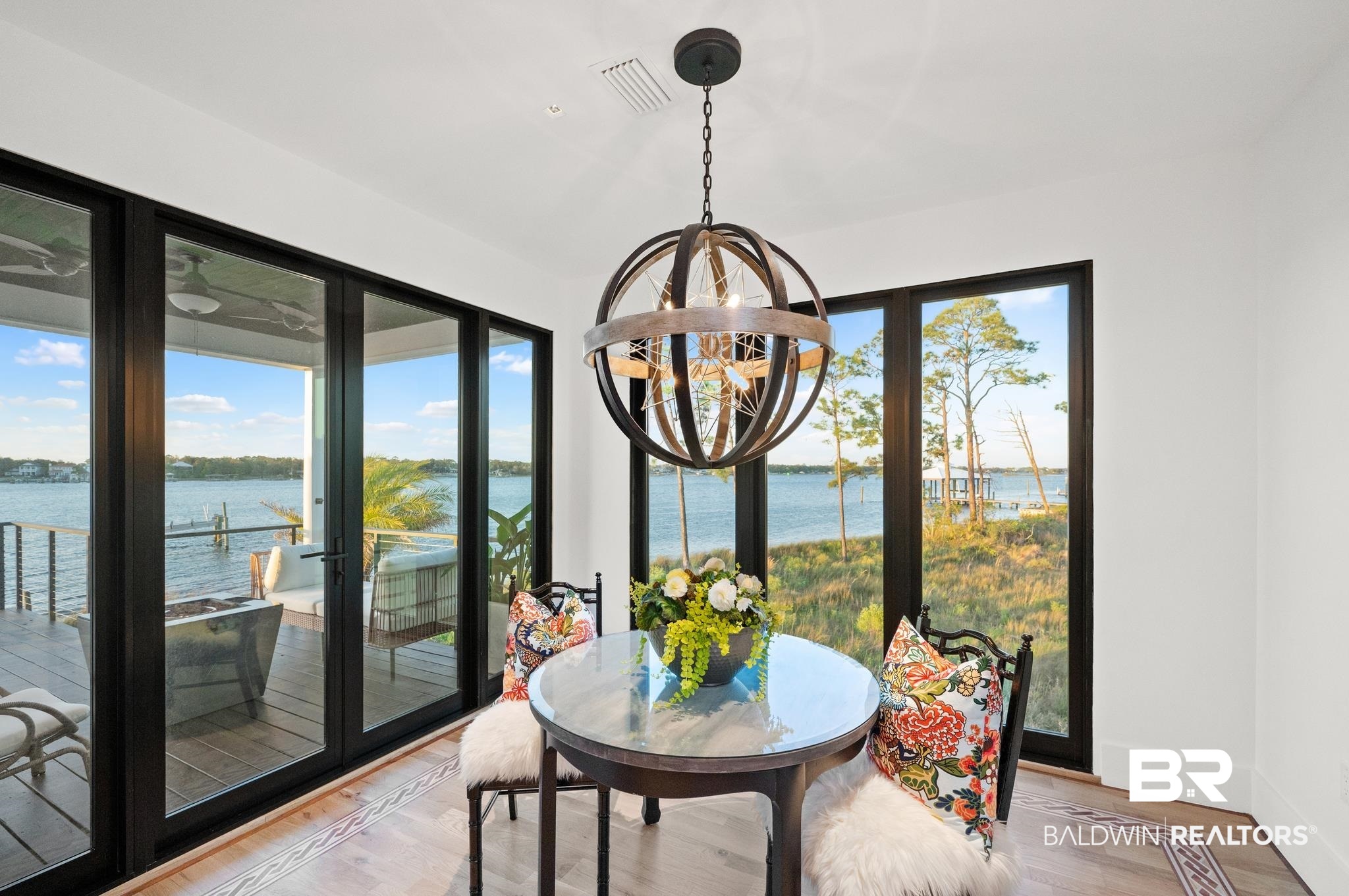 33349 River Road Orange Beach, AL 36561 - Photo 10 of 61 Waterfront dining area featuring expansive glass doors, a round table with a glass top, wood-finish flooring with an inlaid border, and a prominent spherical chandelier