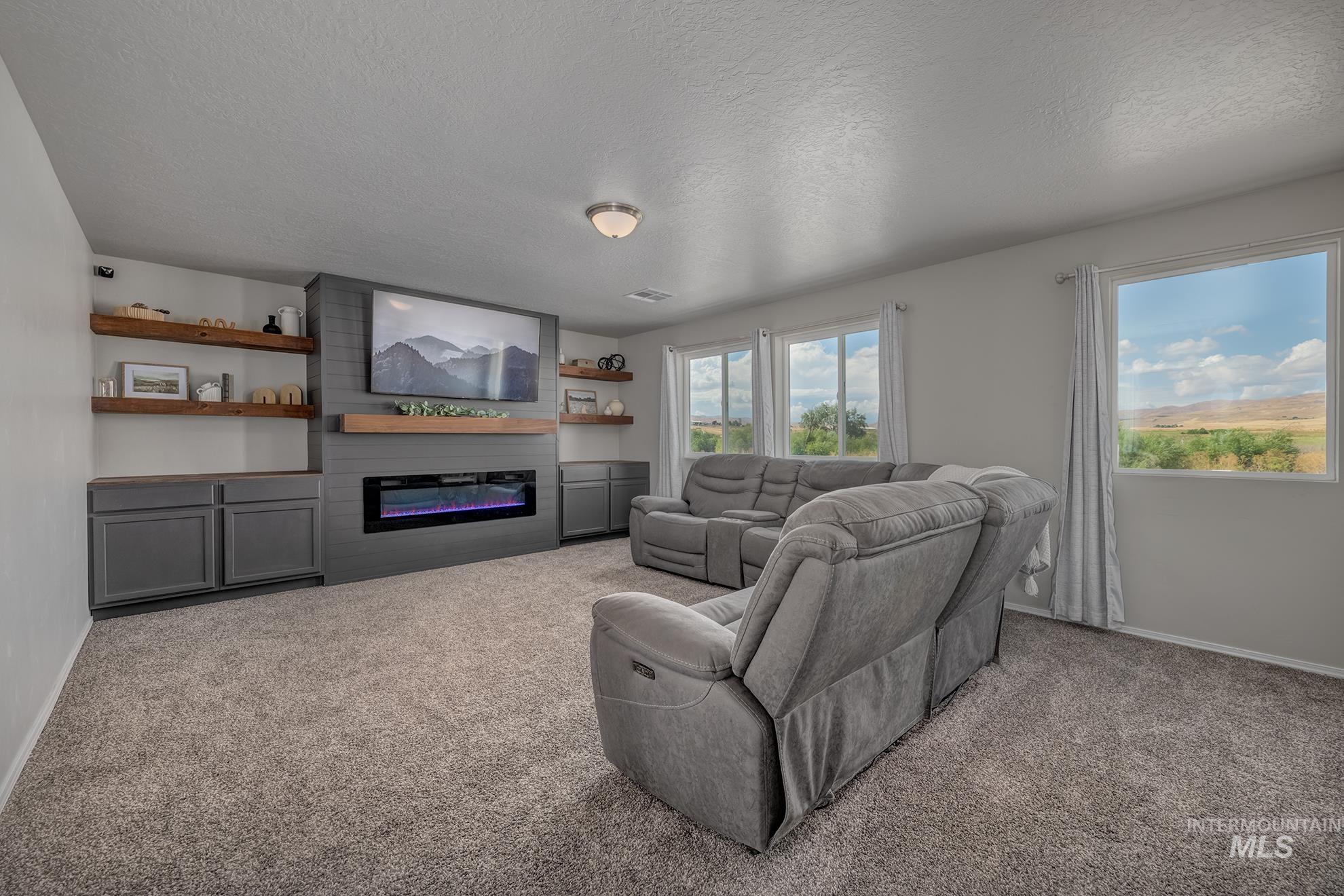 1049 Price Road Weiser, ID 83672 - Photo 20 of 47 Living area featuring a textured gray accent wall with an electric fireplace, a wood-finish mantel, and built-in cabinetry with open shelving