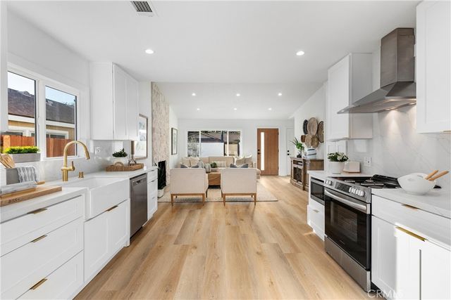 a large kitchen with stainless steel appliances a stove a sink dishwasher and a oven with white cabinets
