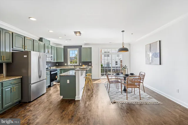 a kitchen with stainless steel appliances granite countertop a refrigerator a microwave a stove and a dining table with wooden floor