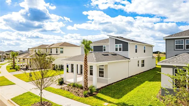 a view of a white house with a big yard plants and large trees