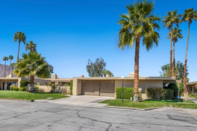 a front view of a house with a garden and palm trees