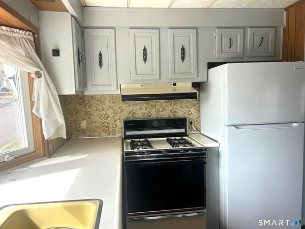 a kitchen with granite countertop a refrigerator a stove and white cabinets with wooden floor