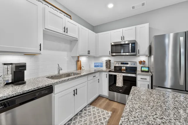 a kitchen with granite countertop a sink stainless steel appliances and white cabinets