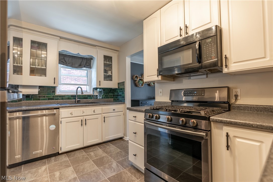 8320 Ackley Road Parma, OH 44129 - Photo 24 of 36 Kitchen featuring stainless steel appliances, tasteful backsplash, white cabinetry, sink, and tile floors