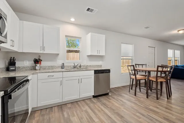 a kitchen with granite countertop white cabinets wooden floor dining table and stainless steel appliances