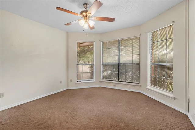 an empty room with chandelier fan and windows
