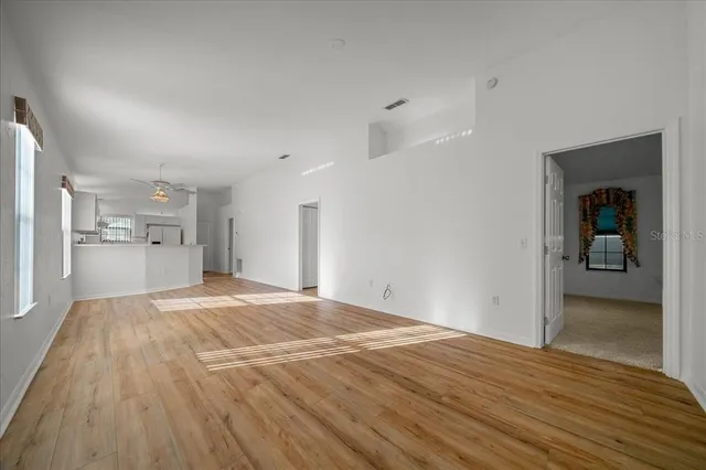 a view of an empty room and kitchen with wooden floor