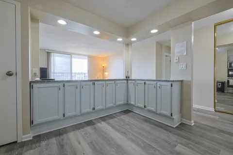 a view of an empty room with wooden floor and a kitchen