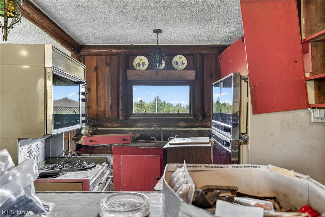 1526 Stevenson Road Ashtabula, OH 44004 - Photo 37 of 50 Kitchen space featuring exposed wood beams, a built-in oven, red cabinetry elements, and a window overlooking exterior greenery