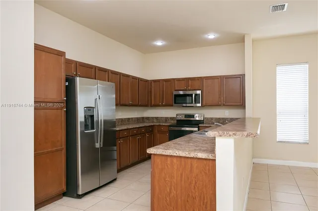 a view of an empty room with kitchen and window