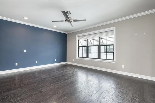 a view of an empty room with wooden floor and a ceiling fan