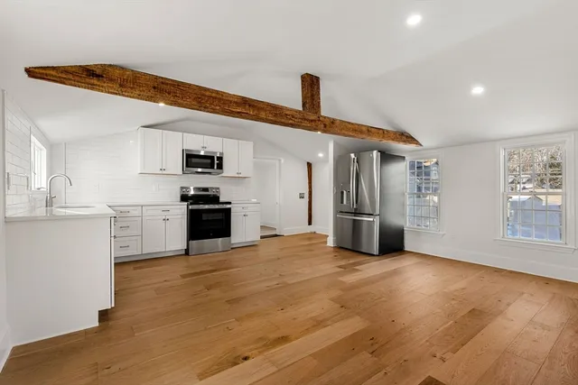 a view of kitchen with stainless steel appliances wooden floor and an empty room