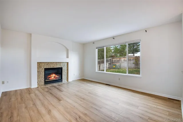 an empty room with wooden floor fireplace and windows
