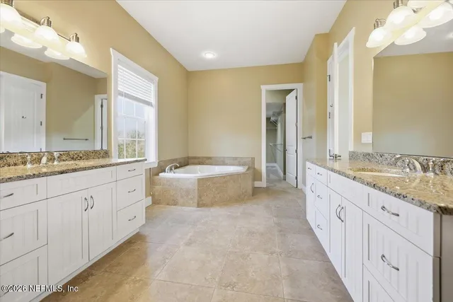 a spacious bathroom with a granite countertop double vanity sink a mirror and a bathtub
