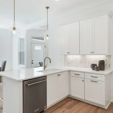 a kitchen with a sink dishwasher and white cabinets with wooden floor