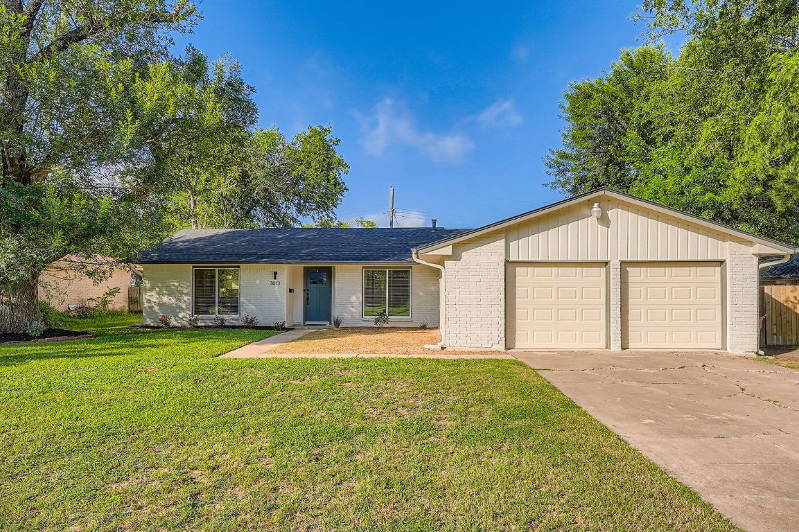 Ranch-style house featuring a garage, brick siding, a front lawn, and driveway