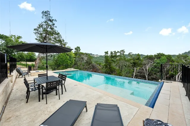 a view of a dining tables and chairs under an umbrella in front of yard