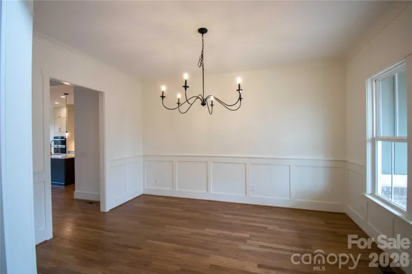 a view of a room with wooden floor chandeliers and kitchen view