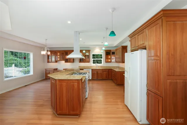 a kitchen with stainless steel appliances granite countertop a refrigerator a sink dishwasher and a dining table with wooden floor