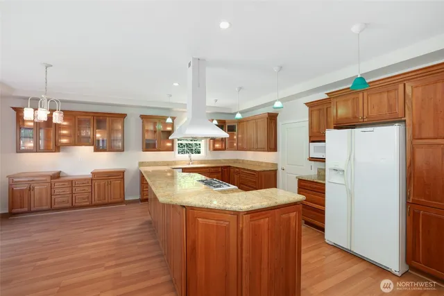 a kitchen with stainless steel appliances granite countertop a sink a stove a refrigerator a center island and a wooden floor