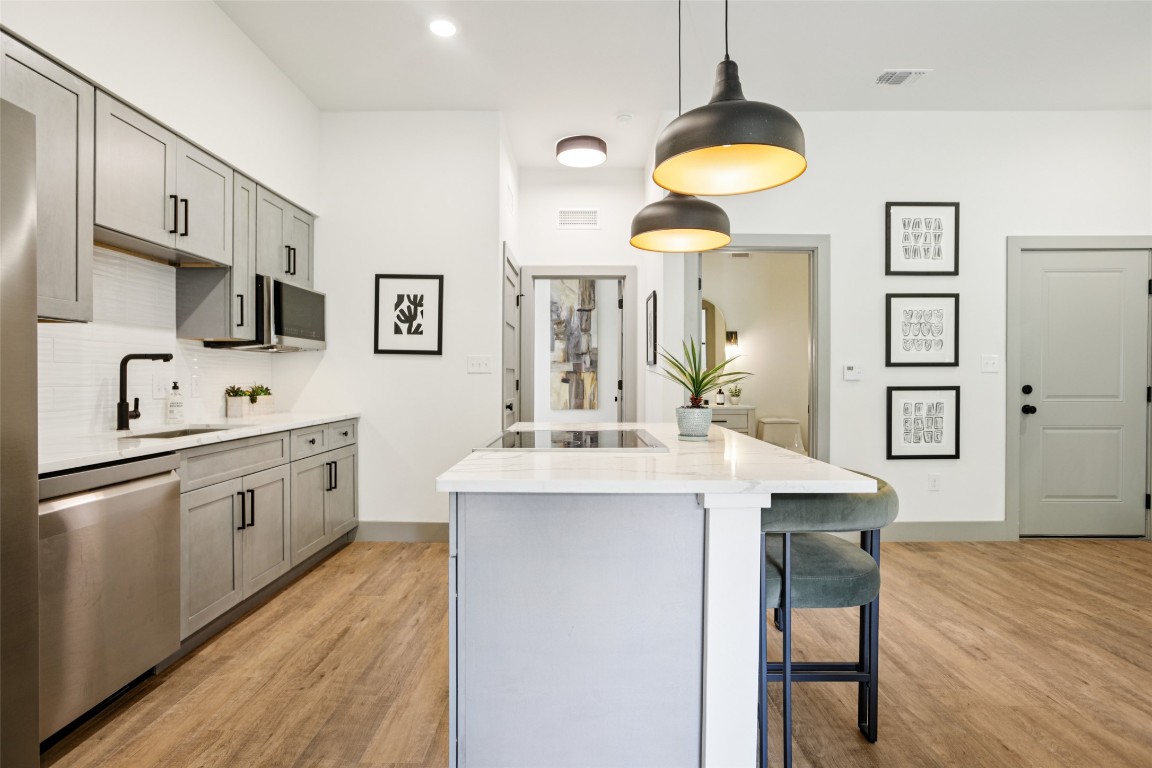 2450 Wickersham Lane, Unit 2023 Austin, TX 78741 - Photo 8 of 27 Kitchen featuring gray cabinets, a center island, light wood-style floors, stainless steel dishwasher, and pendant lighting