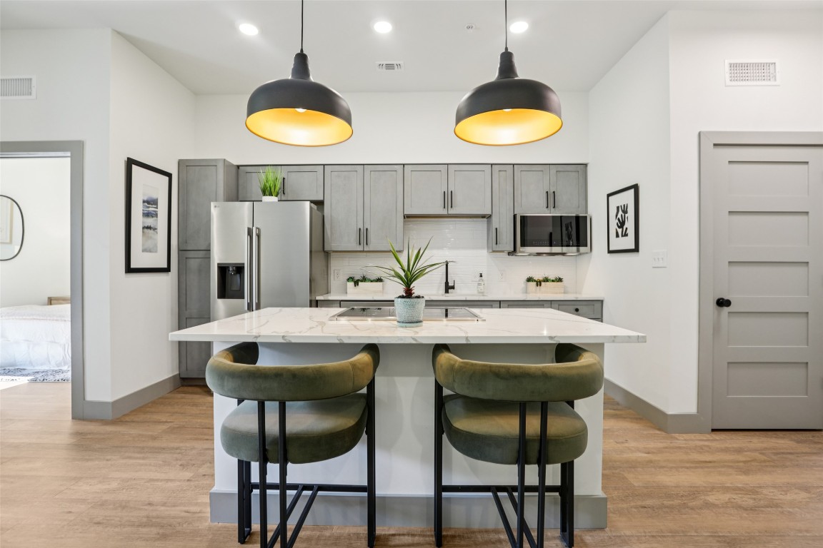 2450 Wickersham Lane, Unit 2023 Austin, TX 78741 - Photo 9 of 27 Kitchen with decorative backsplash, light wood-style floors, hanging light fixtures, a breakfast bar, and light stone counters