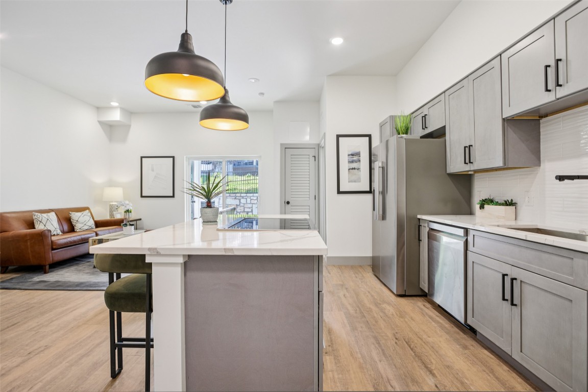 2450 Wickersham Lane, Unit 2023 Austin, TX 78741 - Photo 10 of 27 Kitchen with gray cabinets, hanging light fixtures, a center island, a kitchen bar, and light stone counters