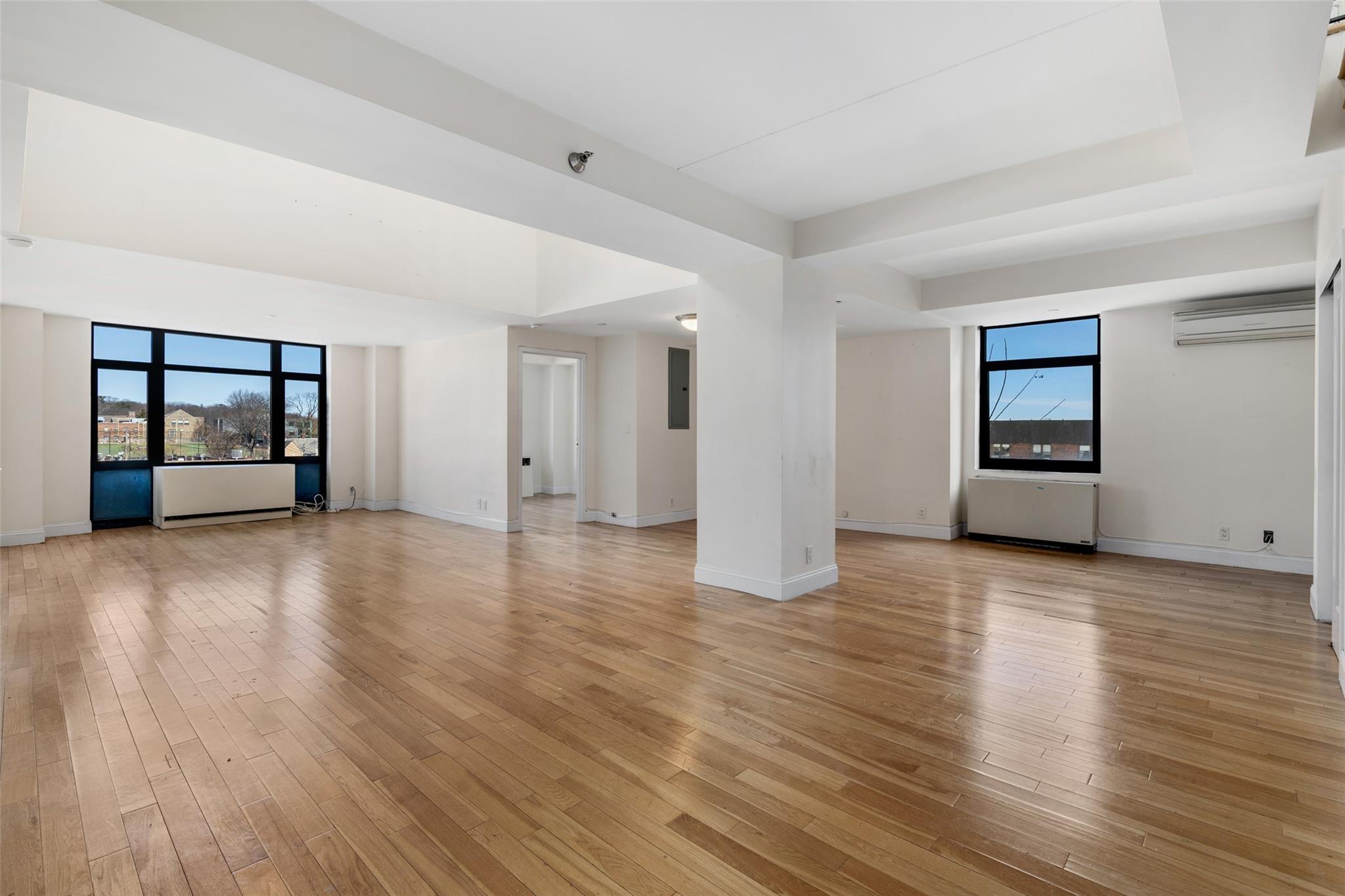Unfurnished living room featuring light wood-style flooring, an AC wall unit, electric panel, and radiator heating unit