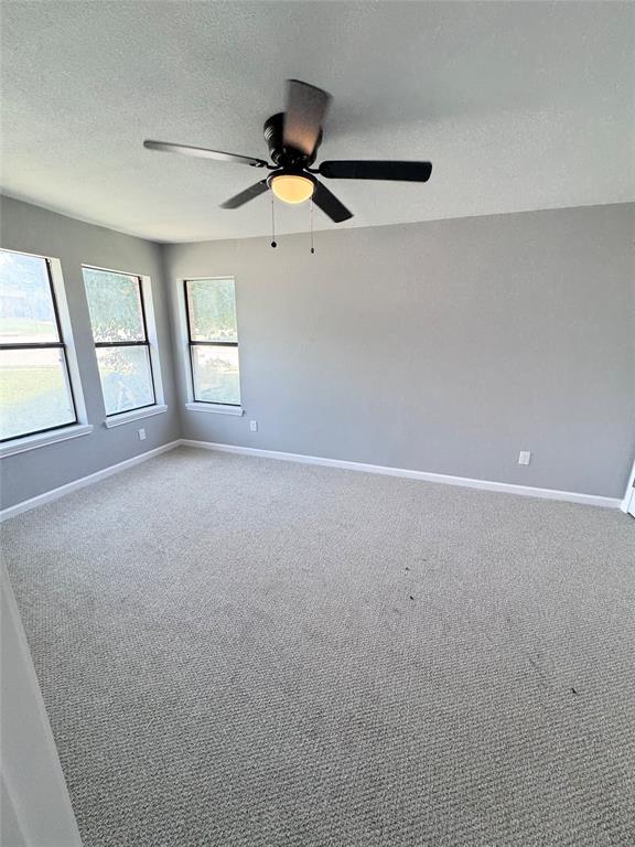 1736 Ransom Terrace Fort Worth, TX 76112 - Photo 21 of 27 Spacious room featuring light gray wall paint, multiple windows, light-toned carpet flooring, white baseboards, and a ceiling fan with light fixture