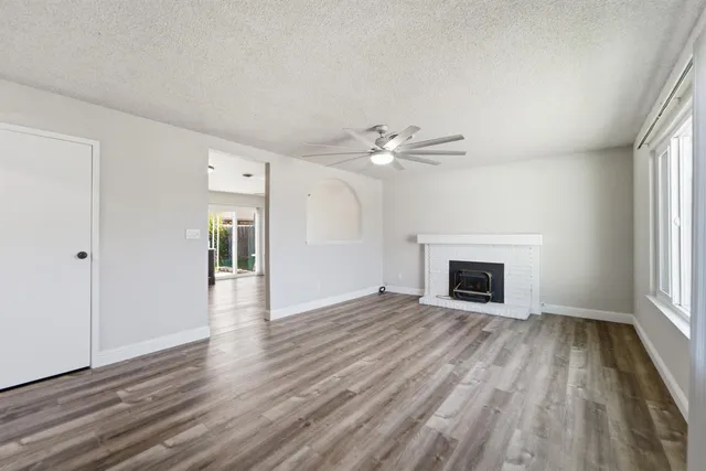 a view of an empty room with wooden floor fireplace and a window