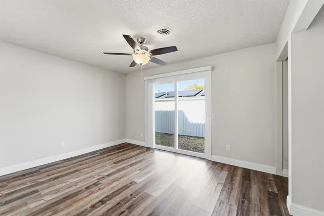 an empty room with wooden floor fan and windows