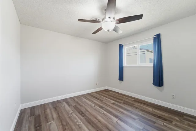 an empty room with wooden floor chandelier fan and windows