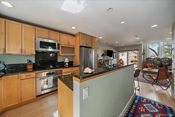 a kitchen with stainless steel appliances granite countertop a stove top oven a sink dishwasher a dining table and chairs with wooden floor