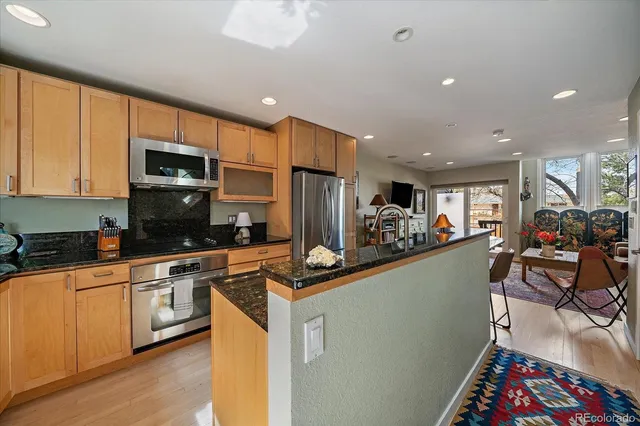 a kitchen with stainless steel appliances granite countertop a stove top oven a sink dishwasher a dining table and chairs with wooden floor