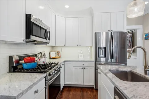 a kitchen with kitchen island granite countertop a stove a refrigerator a sink a center island and chairs with wooden floor