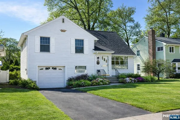 a view of a white house next to a yard with potted plants and large trees