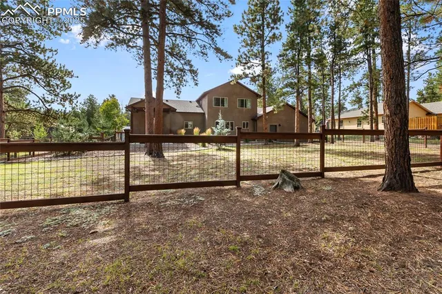 a view of a house with large trees and a wooden fence