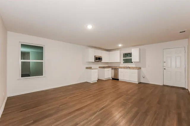 a large white kitchen with kitchen island a sink wooden floor and a refrigerator