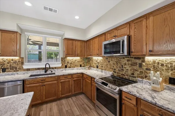 a kitchen with granite countertop a sink dishwasher stove and microwave with wooden cabinets